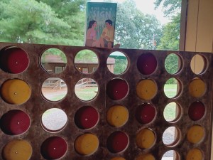 GIVE ME A SIGN perched atop a giant Connect 4 set.